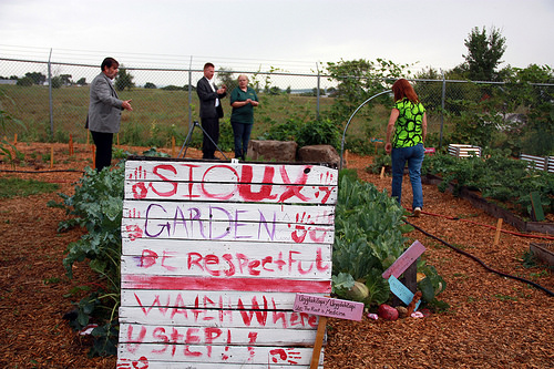 A sign marking the Sioux Garden with people visiting the raised beds of the garden in the background.