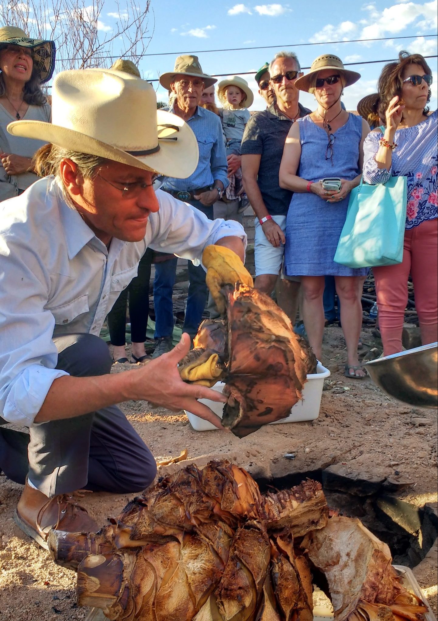 Man holds large roasted agave heart with audience in background